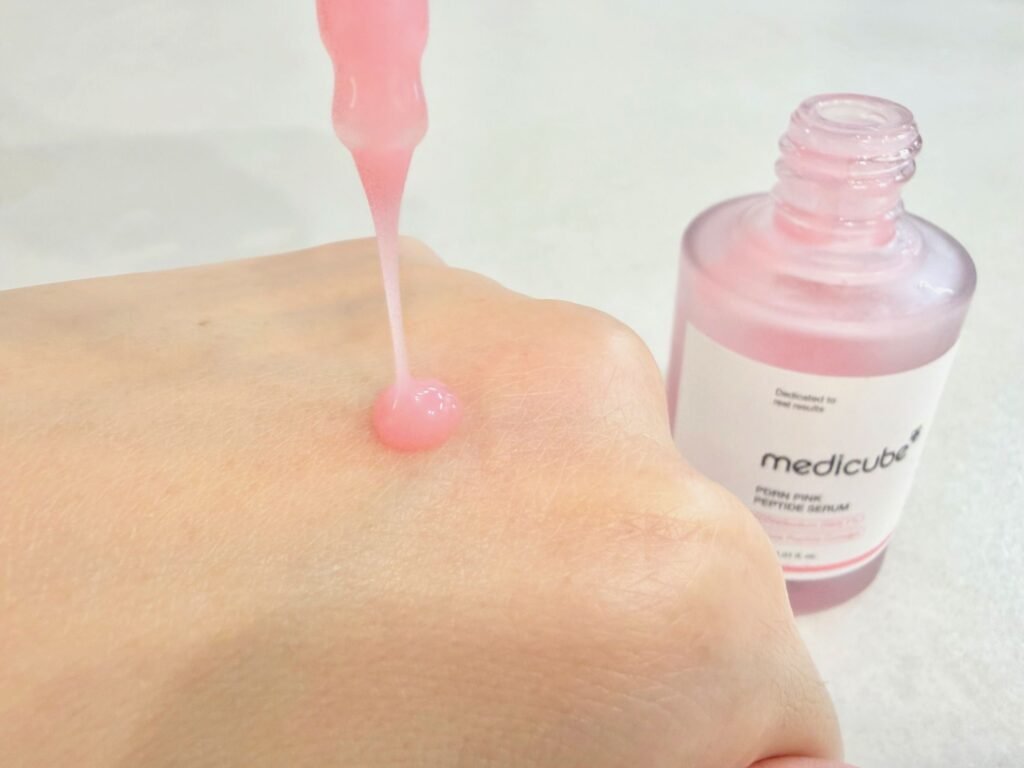 Dispensing bouncy pink serum onto the hand with a dropper next to the Medicube PDRN Pink Peptide Ampoule bottle