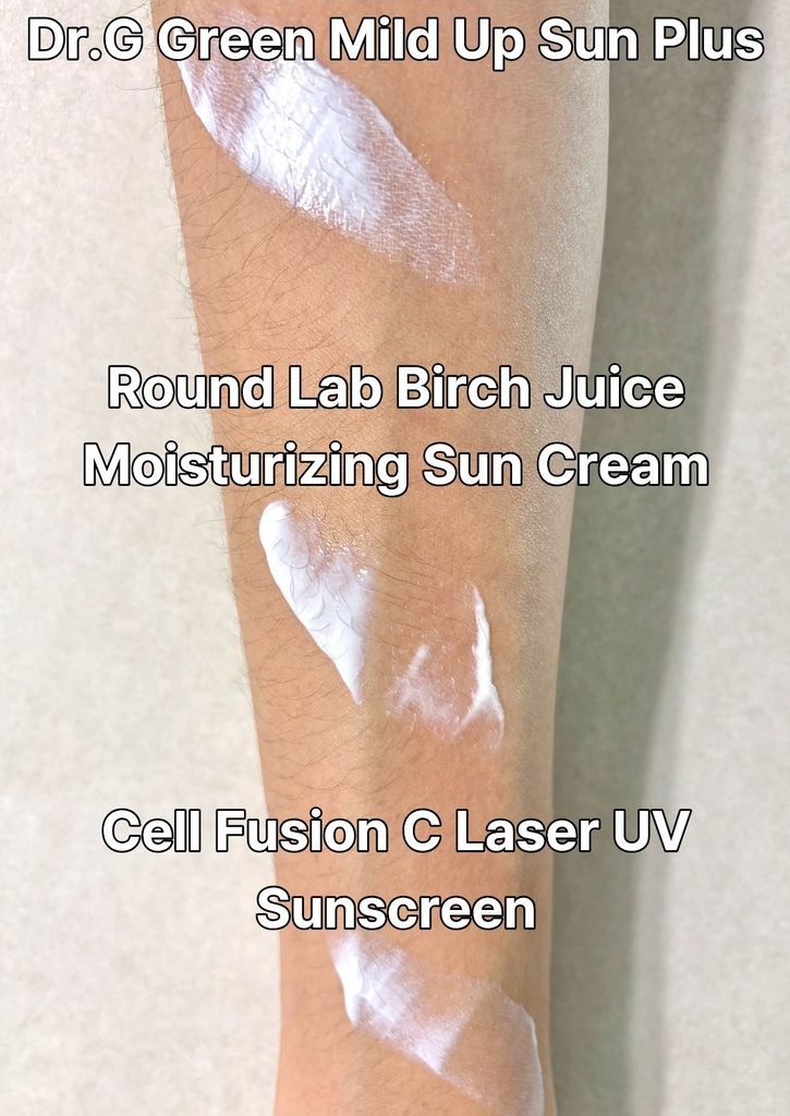 Spreading and testing the textures of Dr.G, Cell Fusion C, and Round Lab sunscreens side-by-side on the arm using a metal spatula.