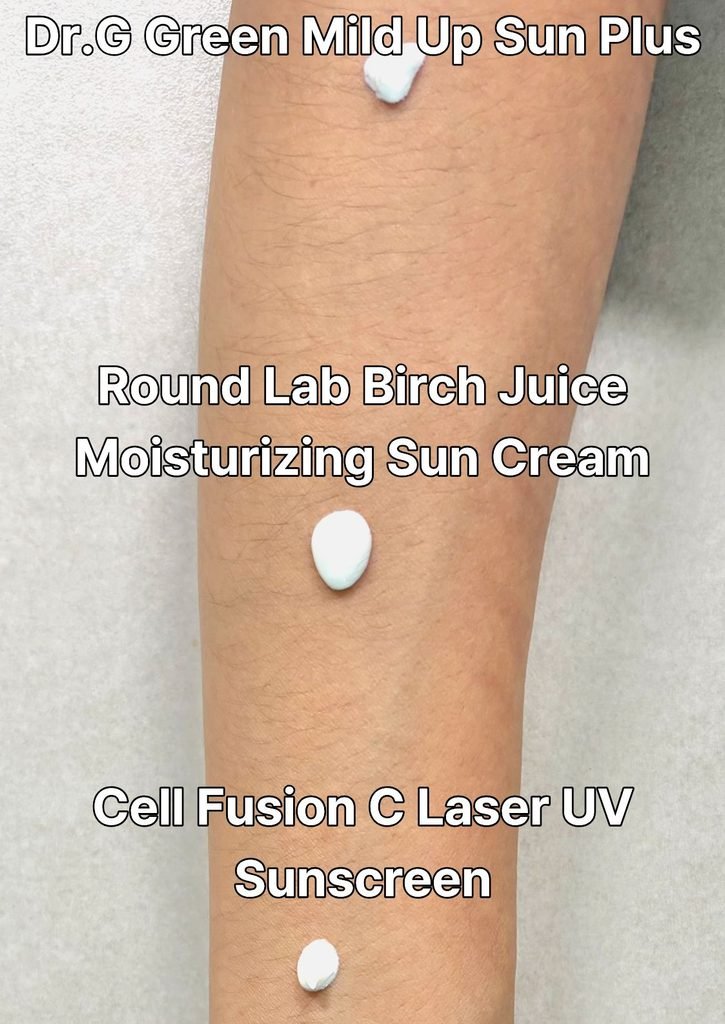 Three distinct dollops of K-beauty sunscreen formulas—Dr.G, Cell Fusion C, and Round Lab—squeezed side-by-side in a line on a person's forearm for a texture comparison test.