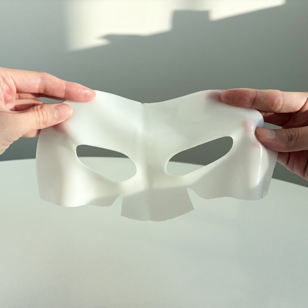 Holding the thick, milky-white hydrogel upper sheet of the Biodance Bio-Collagen Real Deep Mask before application.
