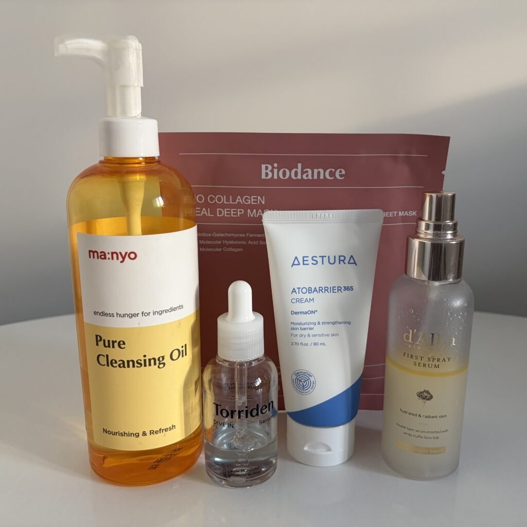 Curated October Prime Day K-Beauty routine lineup featuring Manyo Cleansing Oil, Torriden Serum, Aestura Cream, d'Alba Mist, and Biodance Mask on a vanity table.