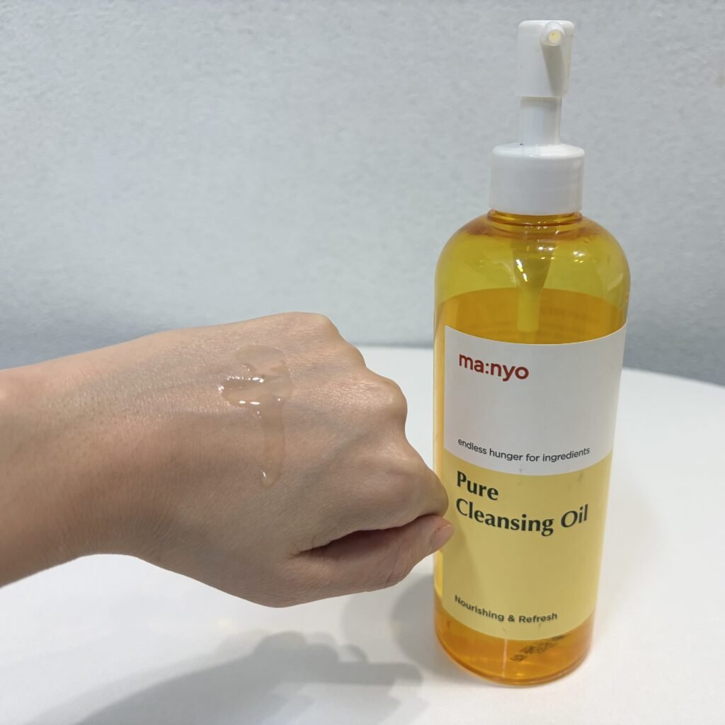 Lightweight golden Manyo Pure Cleansing Oil running down the back of a hand with the yellow oil bottle visible in the background
